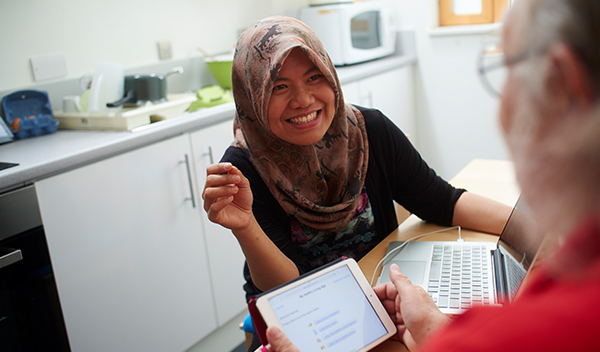 A woman at table smiling with a man on a tablet