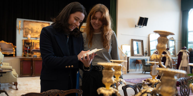 Two students looking at some plates together, with art in the background.