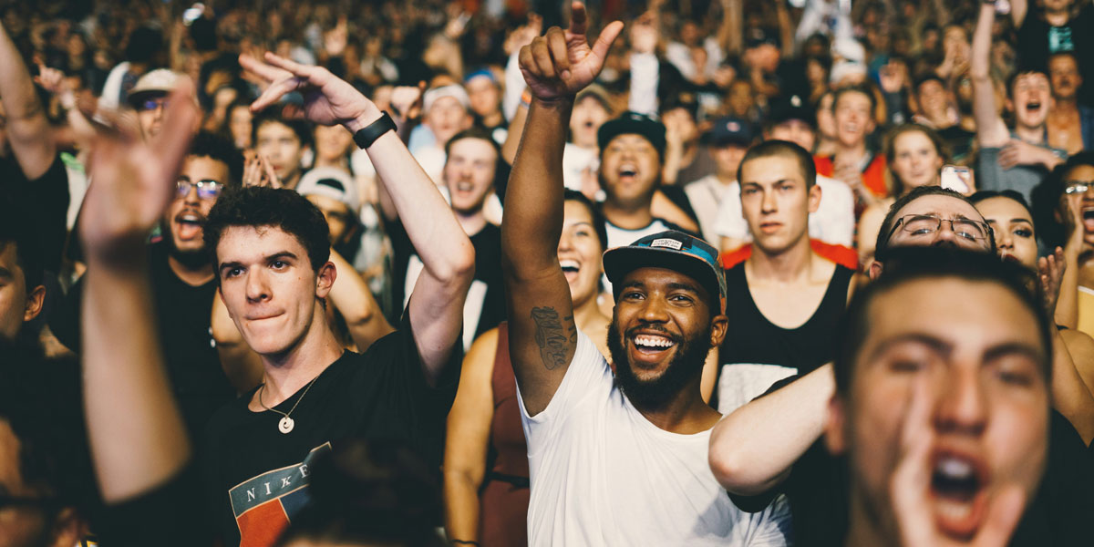 A smiling audience at a rock concerts with arms raised as they listen to music. Nicholas Green on Unsplash