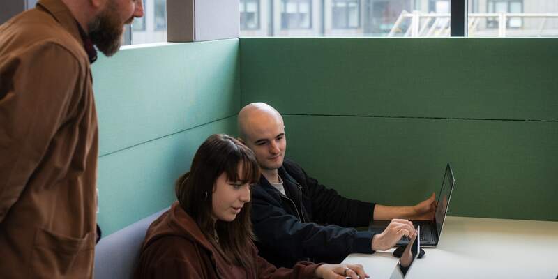 students working on laptops and demonstrating their work to a supervisor